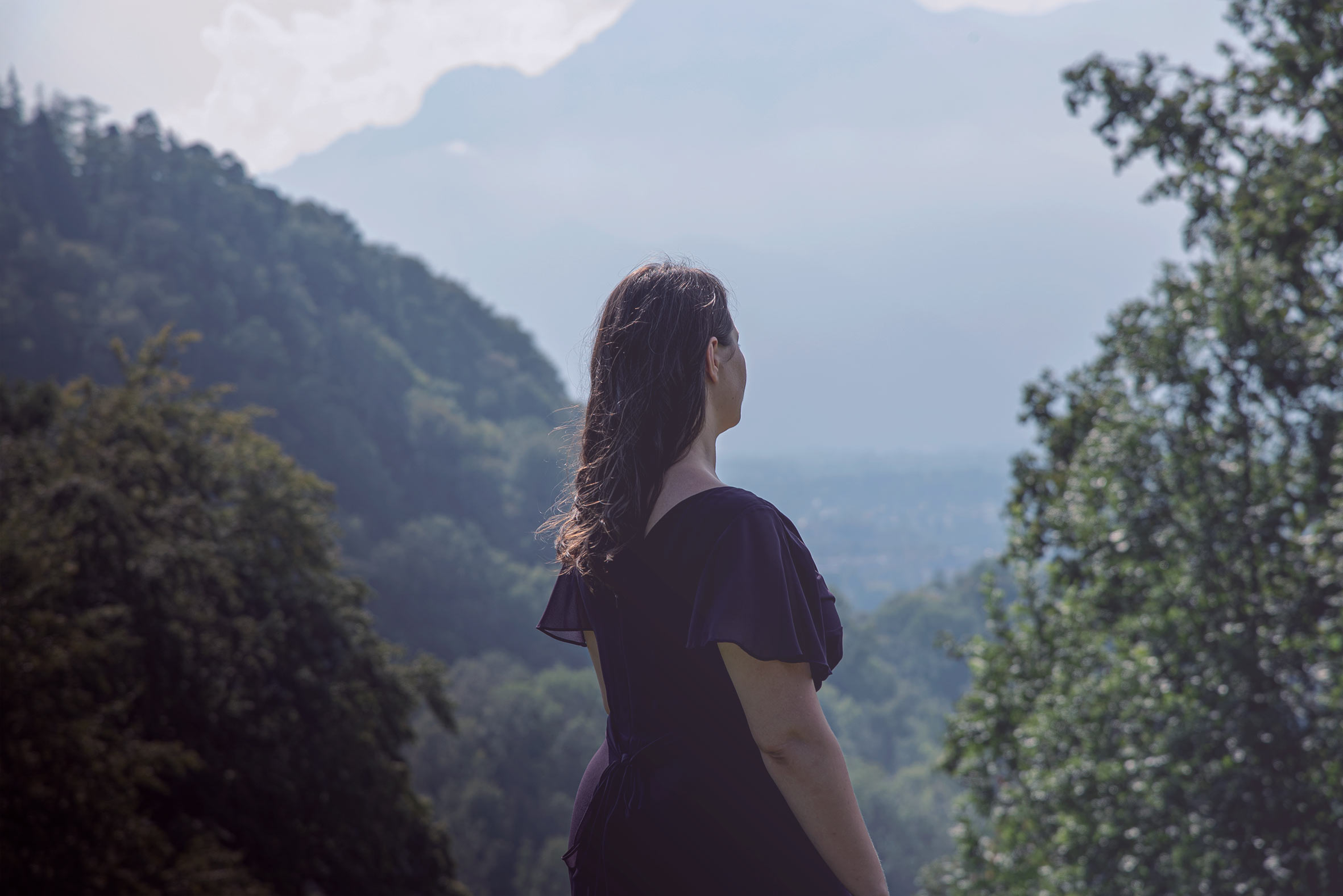 Eine Frau mit dunklem Haar blickt in der Stimmwerkstatt Salzburg auf bewaldete Berghänge und ein weites Tal.