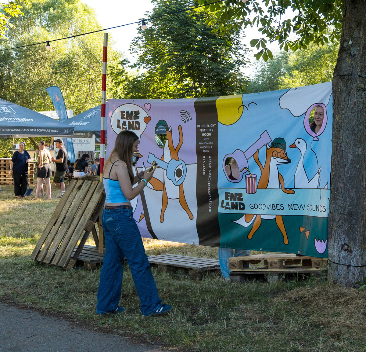 Buntes Banner mit dem Enzland-Logo und Illustrationen von Figuren auf einem Festival.